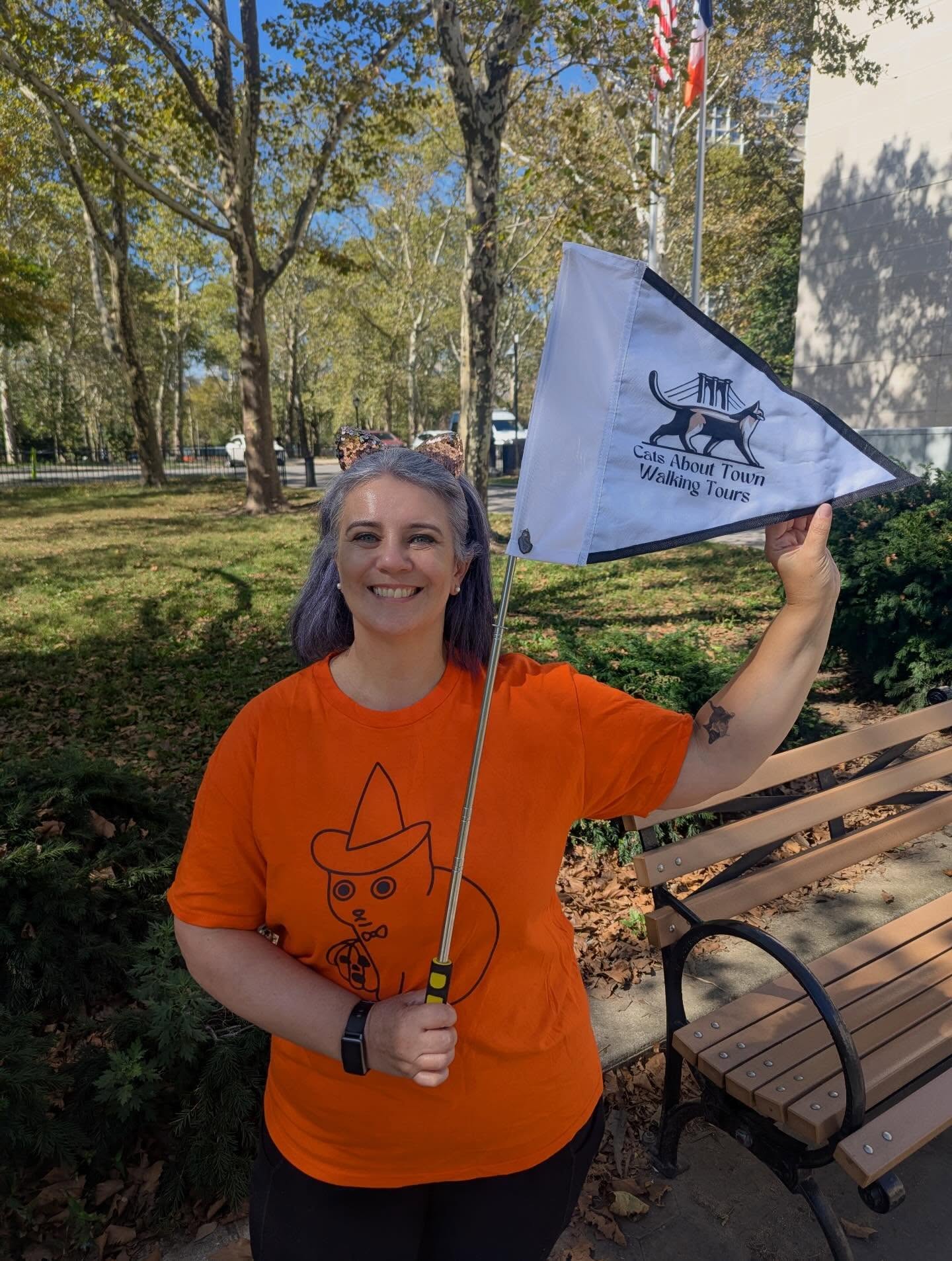Tour guide Marie holding Cats About Town Walking Tours flag in park
