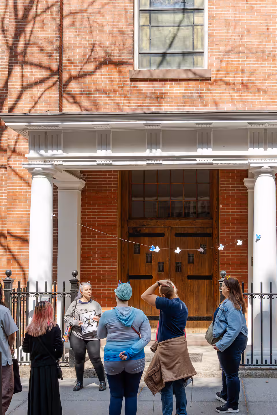 Tour group listens to the guide in front of a Brooklyn Heights brick townhouse with a white portico