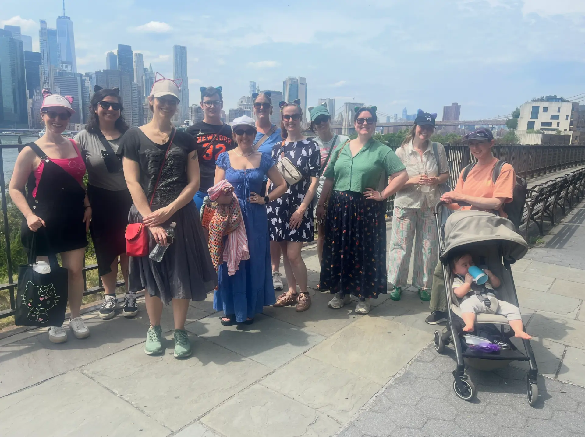 Cats About Town tour group posing on the Brooklyn Heights Promenade with the Manhattan skyline and Brooklyn Bridge behind them