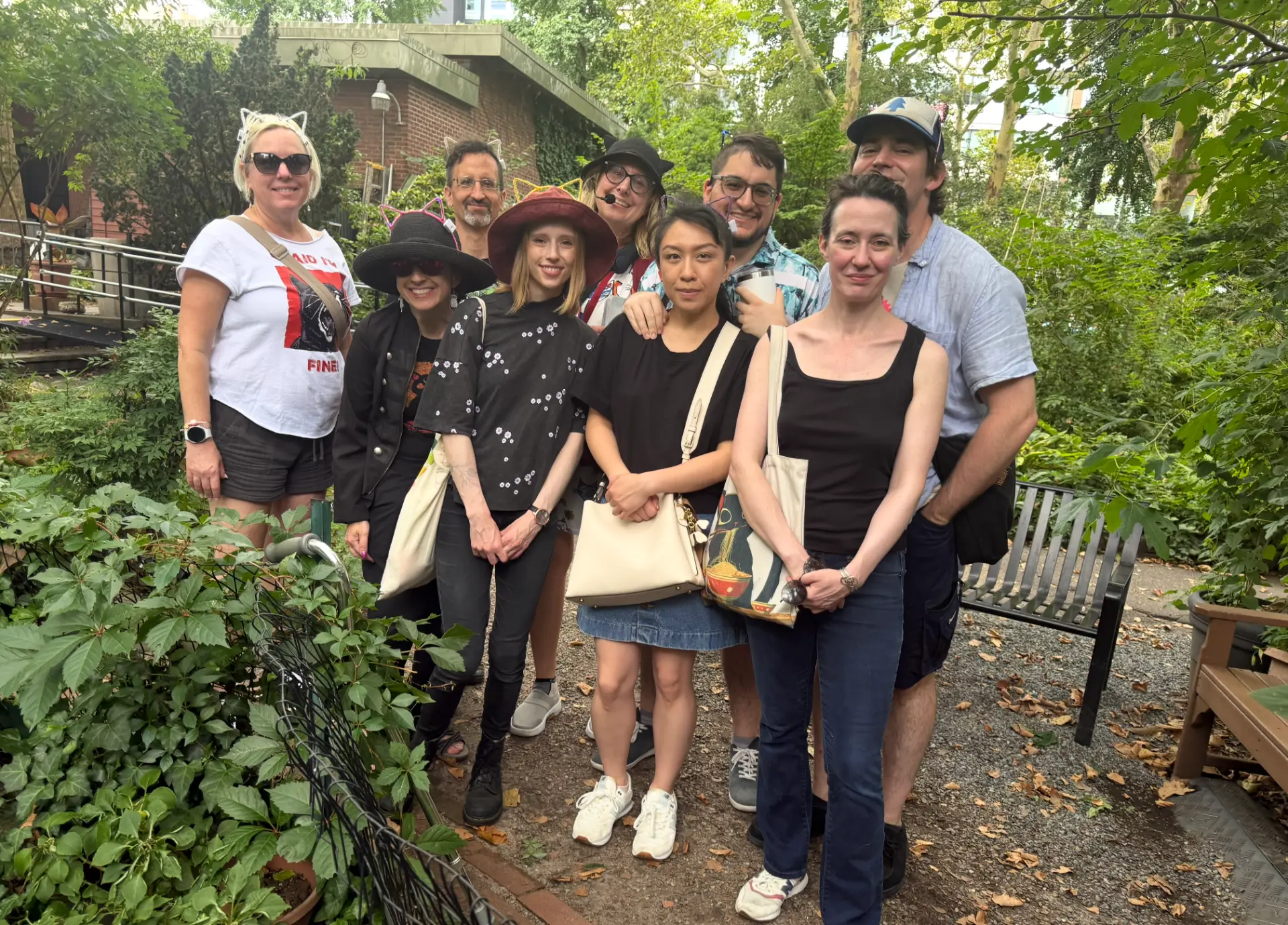 Cats About Town tour group wearing cat ears gathered in a leafy Manhattan community garden