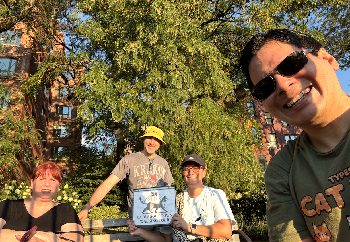 Tour guests smiling for a group photo with the Cats About Town Walking Tour sign in a Brooklyn park
