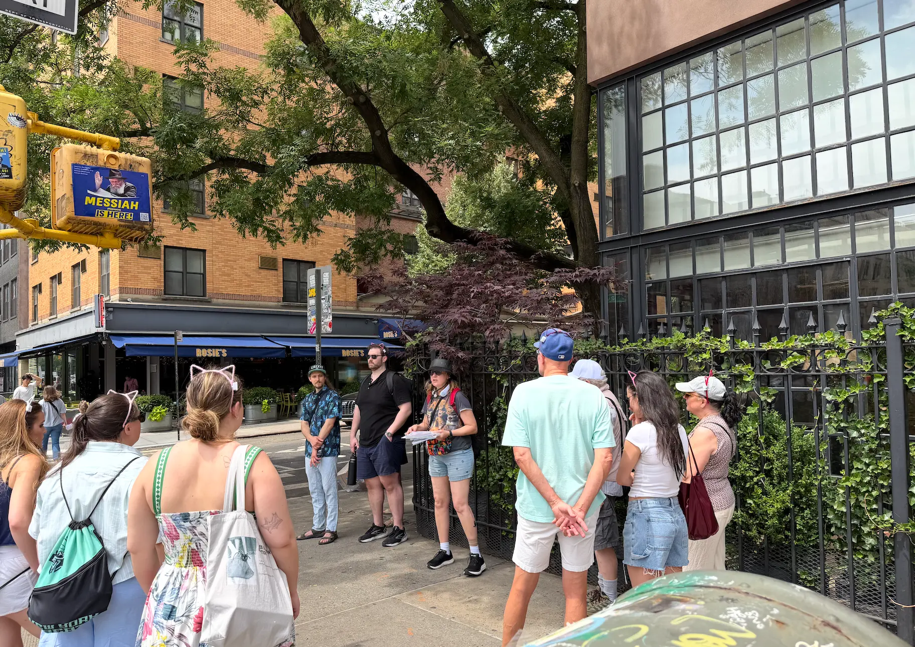 Tour group in cat ears listens to the guide at a leafy downtown Manhattan street corner