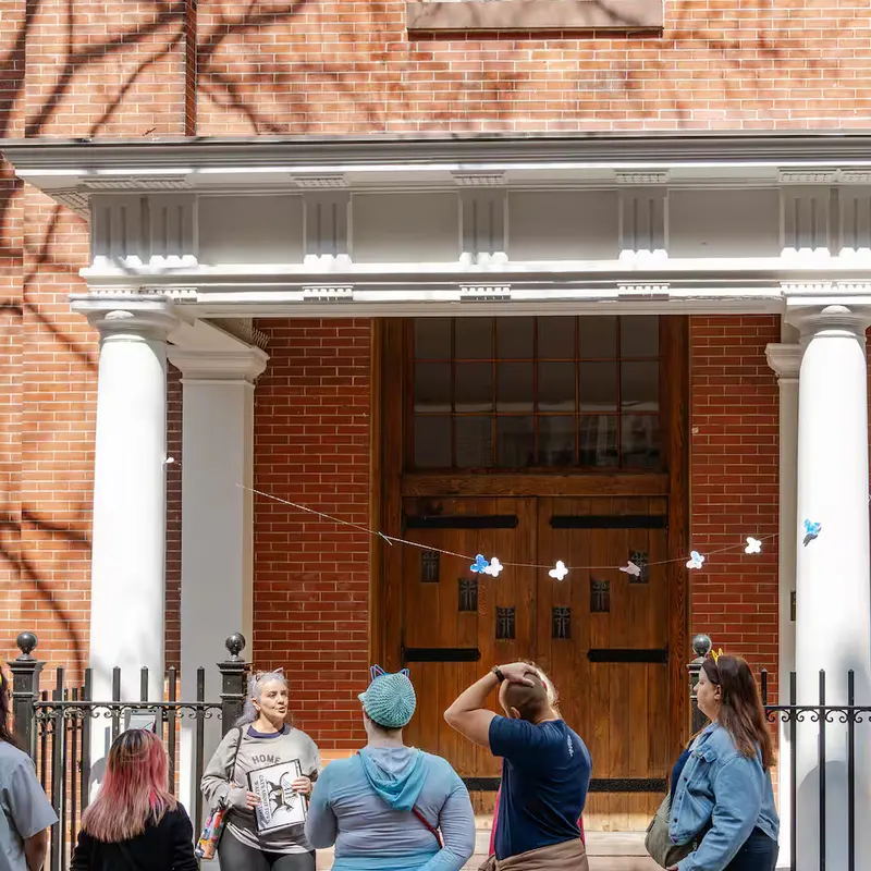 Cats About Town tour group listens to the guide in front of a brick townhouse with a white portico