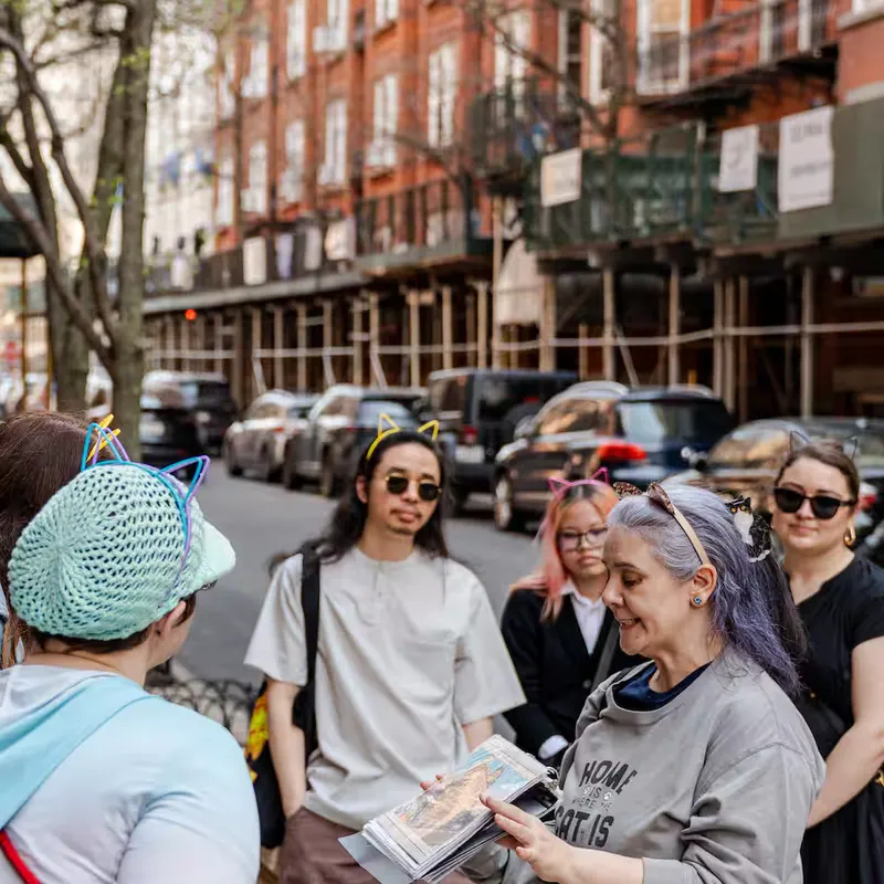 Guide shows vintage cat photos from a binder while guests in cat ears listen on a Brooklyn street