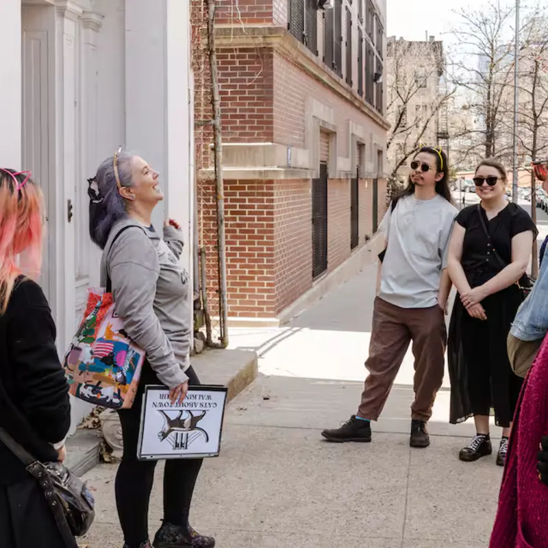 Guide with purple hair leads a Cats About Town walking tour group on a sunny Brooklyn Heights sidewalk