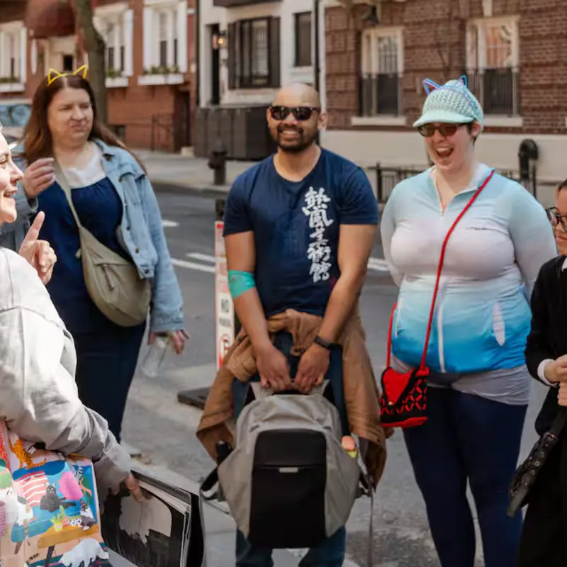Tour guide shares historic cat photographs with guests wearing cat-ear headbands on a Brooklyn Heights street